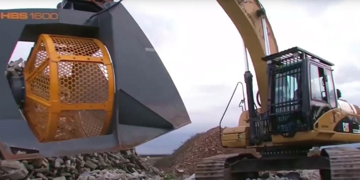 Excavator with a screening bucket sorting rocks and debris on a construction site